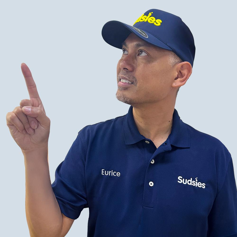 Sudsies team member Eurice pointing upward while wearing a branded uniform and cap.
