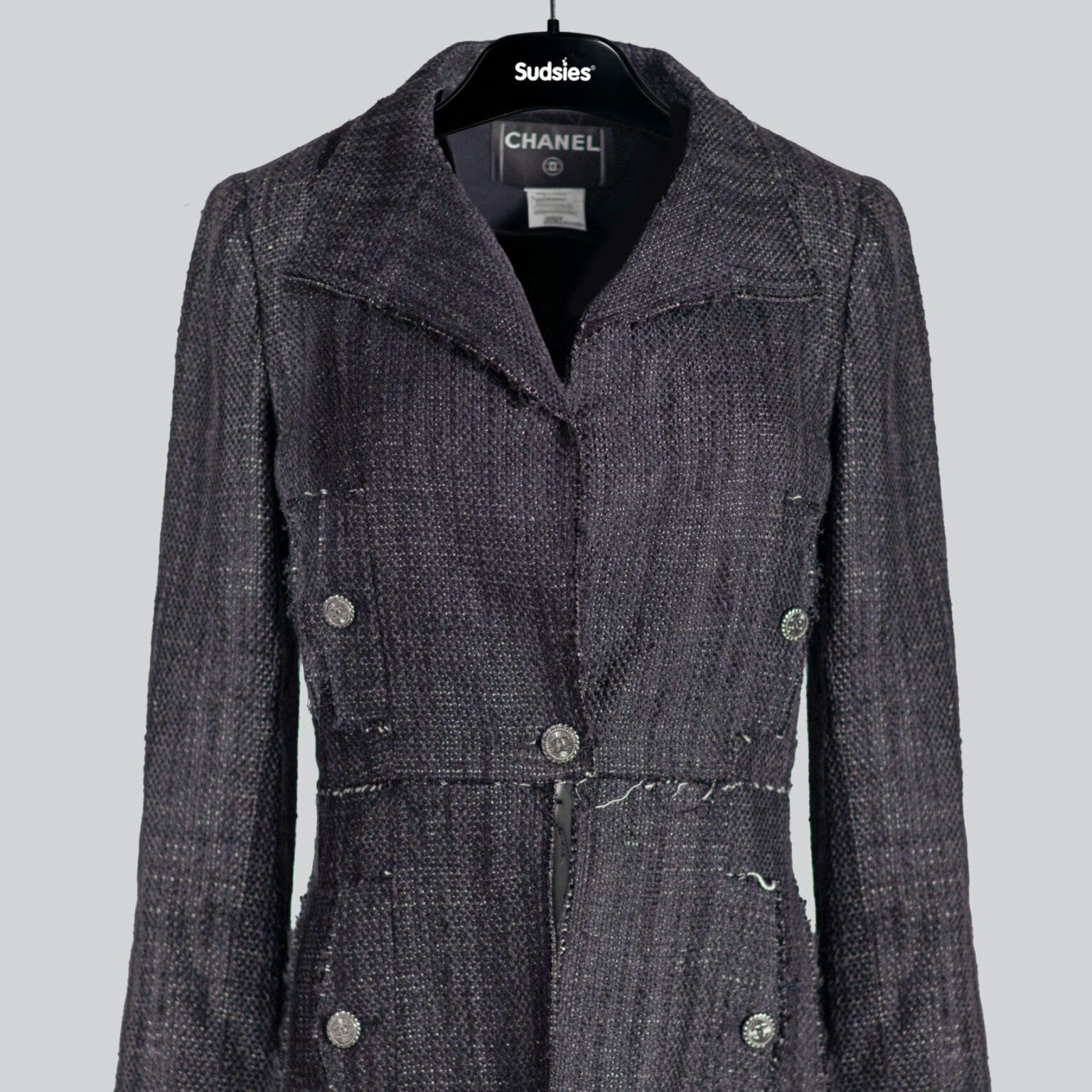 A dark grey Chanel linen jacket with silver buttons, displayed on a black Sudsies hanger against a light grey background.