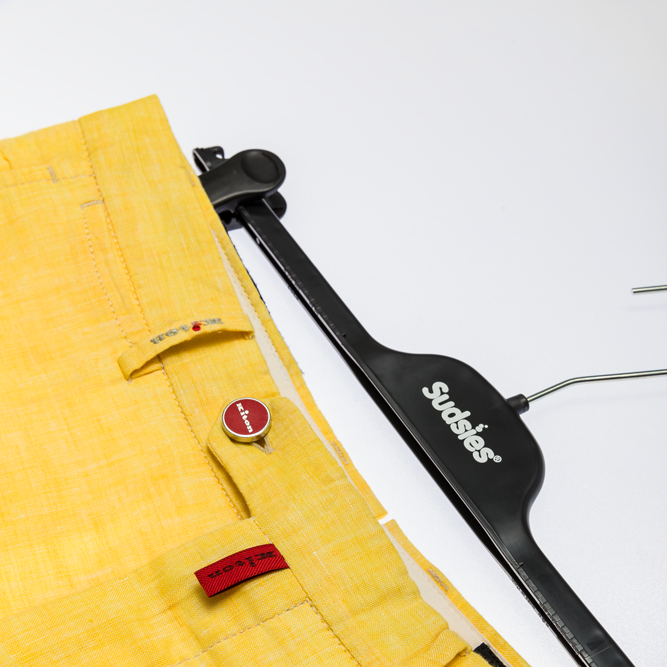 Close-up of bright yellow Kiton shorts resting beside a black Sudsies hanger on a white surface.