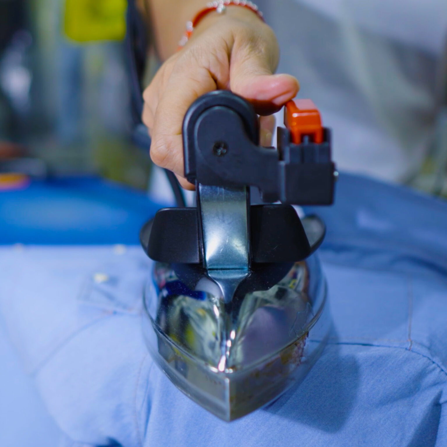 Close-up of a technician pressing a blue dress shirt with a professional-grade steam iron, hand gripping the handle with focused precision.