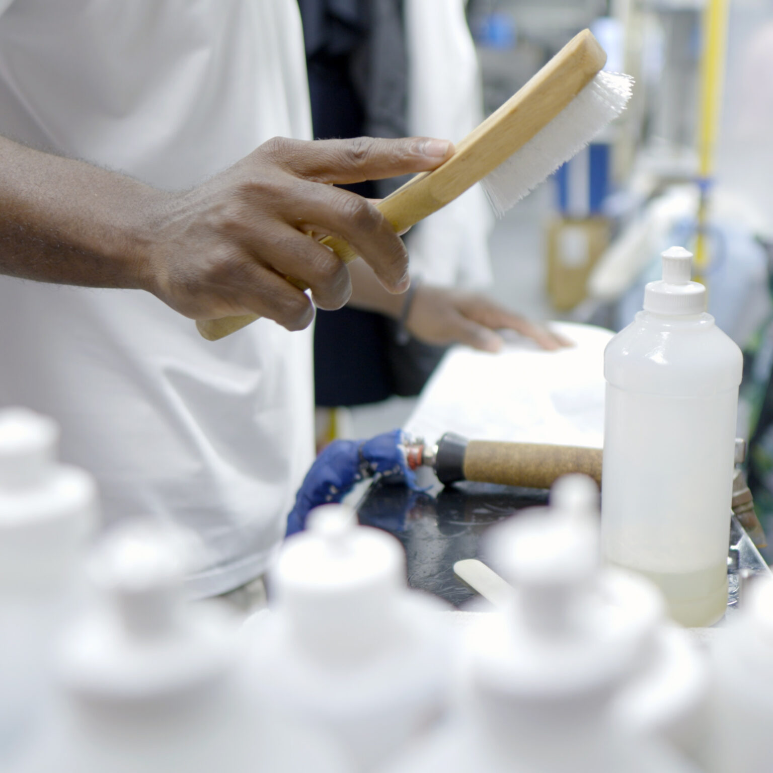 Close-up of a technician’s hand holding a garment brush above a workstation with multiple cleaning solution bottles and spot treatment tools.