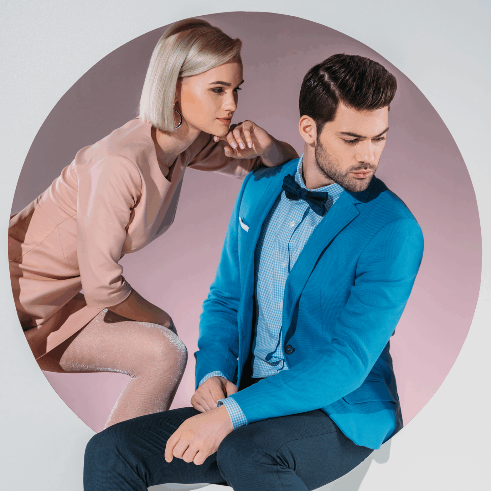 Stylish woman in a blush pink dress and man in a bright blue blazer with bow tie pose together inside a circular cutout set against a gradient pink background, evoking high-fashion editorial energy.